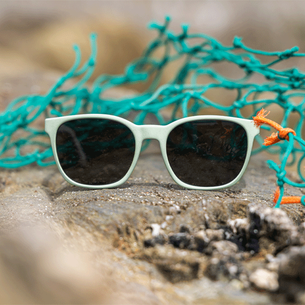Green sunglasses with grey lenses on a rocky surface with green fishing net in the background