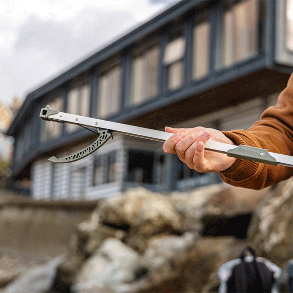 Person holding a metal litter picker tool outdoors with a building in the background