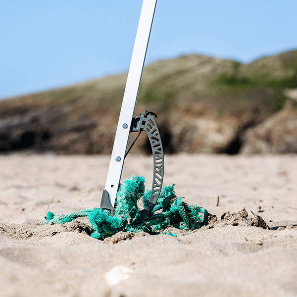 Metal litter picker tool with green rope on sandy ground against a natural background