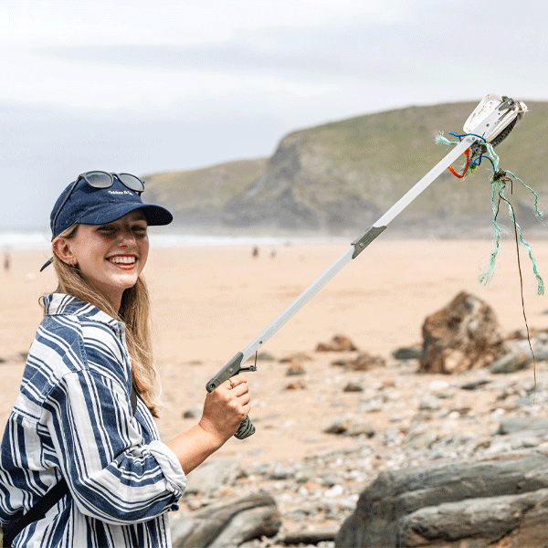 Woman on a beach holding a litter picker with a scenic background