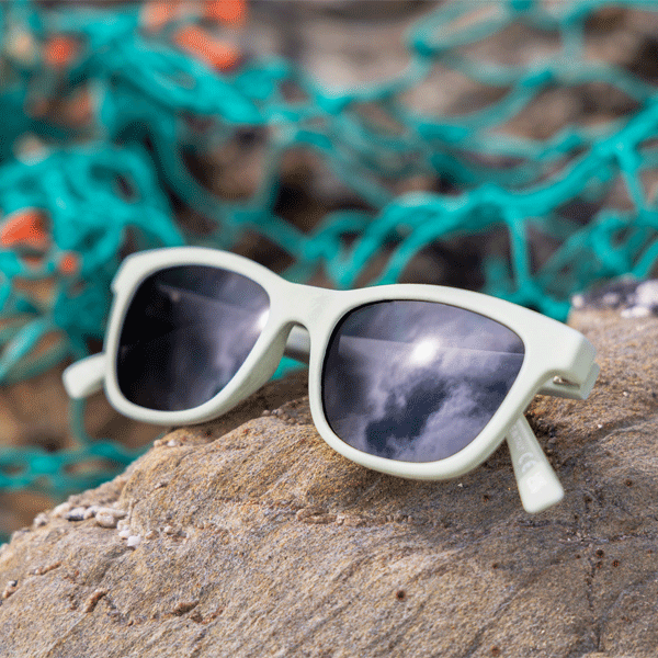 Sunglasses with reflective lenses on a rock with blurred green netting in the background