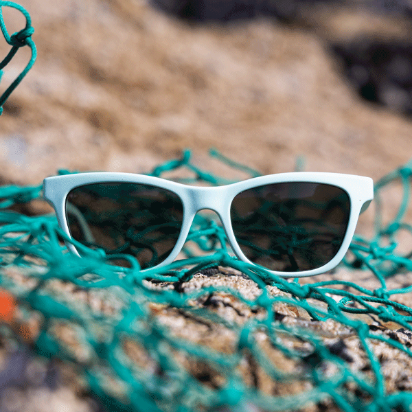 White sunglasses with dark lenses on a textured surface with green fishing net