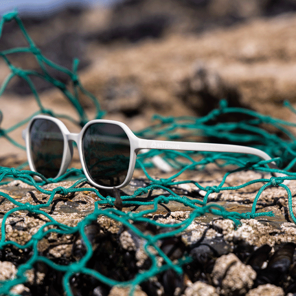 White sunglasses with dark lenses on a piece of green fishing net.