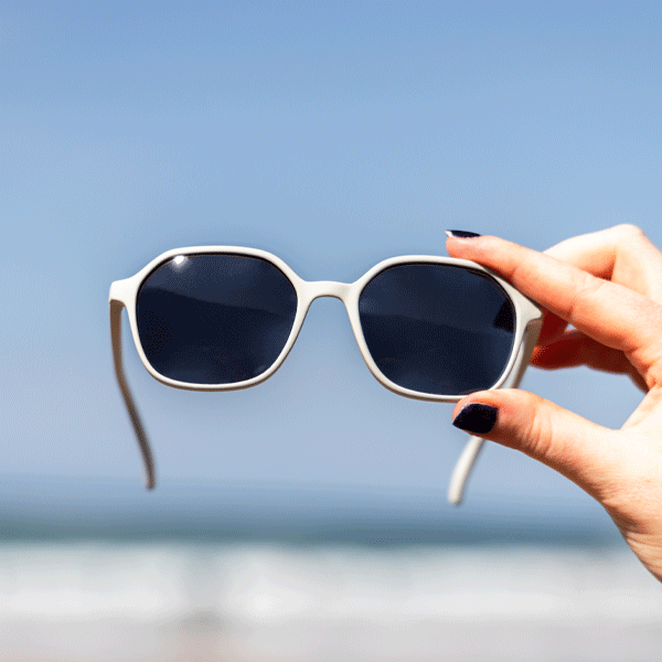 Sunglasses held by a hand against a blue sky