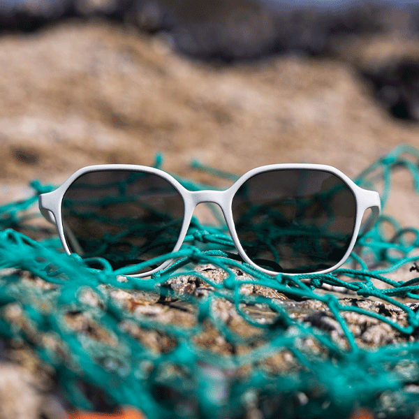 Sunglasses with white frame and dark lenses on a piece of green fishing net with a blurred natural background