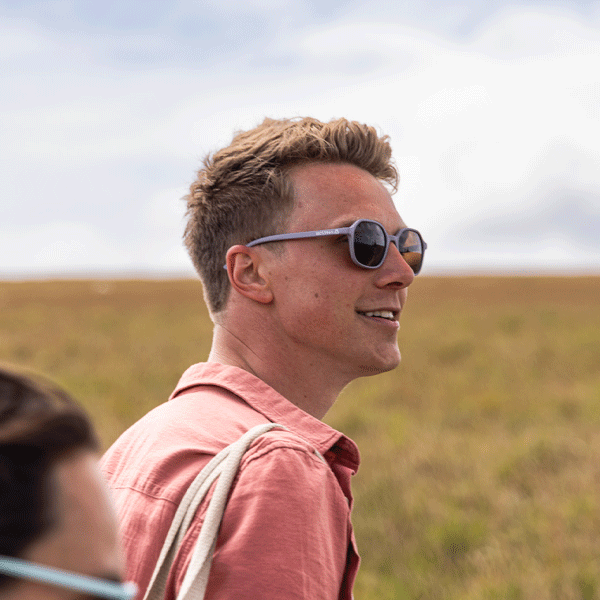 Man wearing sunglasses and a pink shirt standing in a field