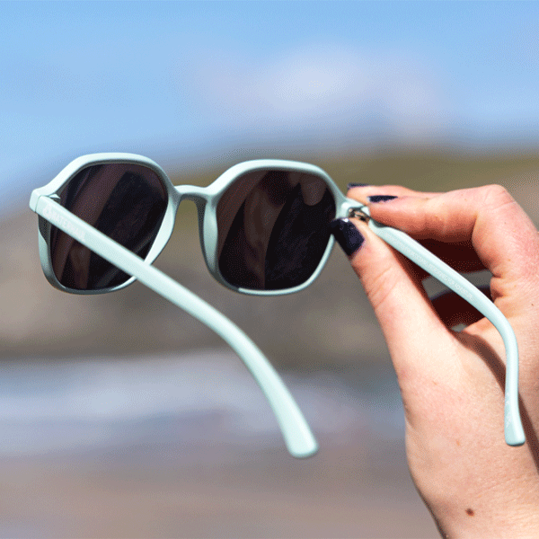 Hands holding light blue sunglasses up against sky and natural background