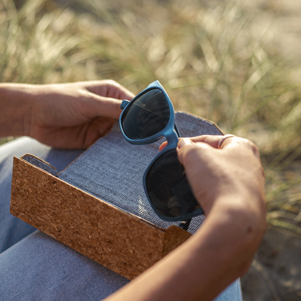 Navy sunglasses being removed from a cork sunglasses case with a natural background