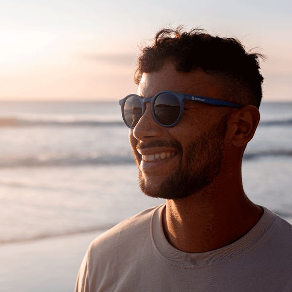 Man wearing blue round sunglasses on a beach at sunset
