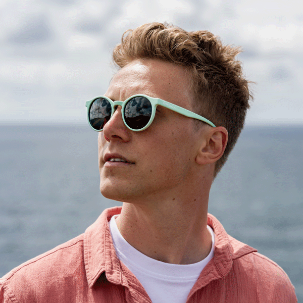 Man wearing sunglasses with a pink shirt against a cloudy sky