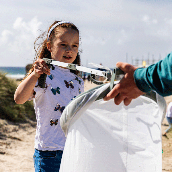 Child holding a litter picker on a beach with an adult assisting