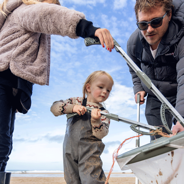 Family with a child using litter pickers on a beach on a sunny day.
