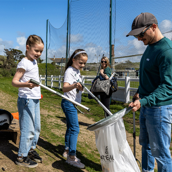 Two children and a man participating in a beach clean-up activity with litter pickers and trash bags.