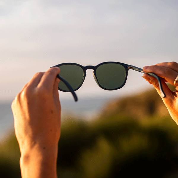 Hands holding up a pair of sunglasses to the sun