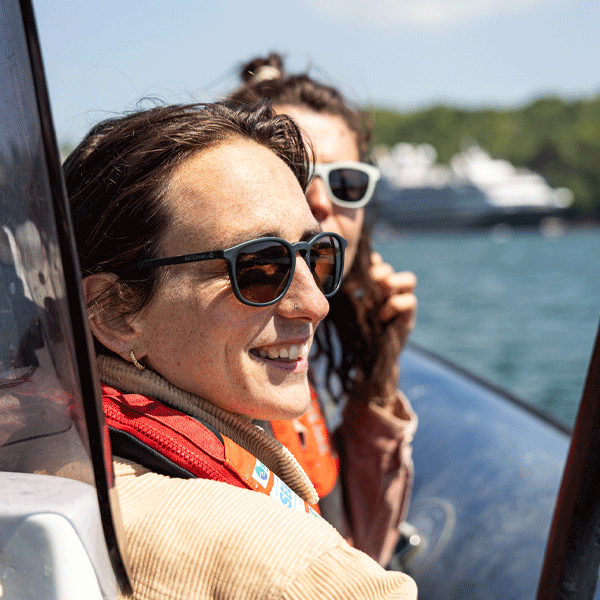 Two people on a boat with sunglasses, smiling, and looking out at water.