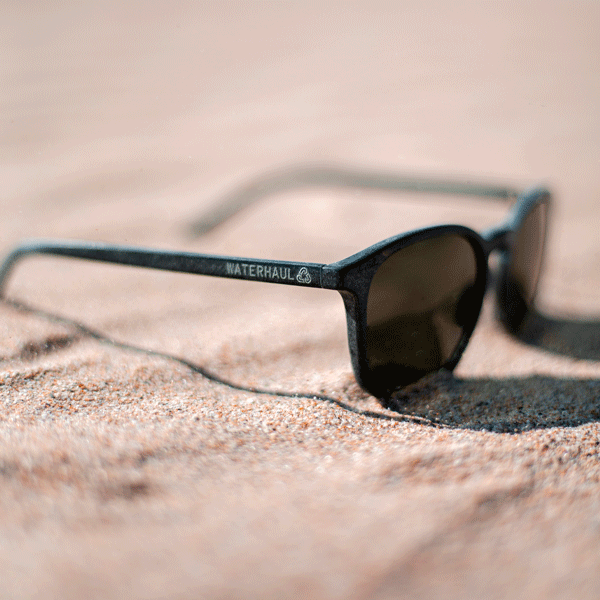 Sunglasses with 'WATERHAUL' branding on a sandy surface