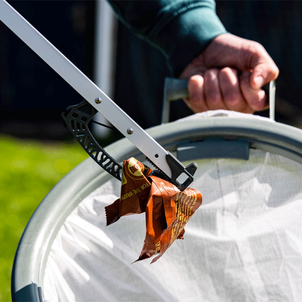 Person using a litter picking tool to put litter in a white trash bag underneath.