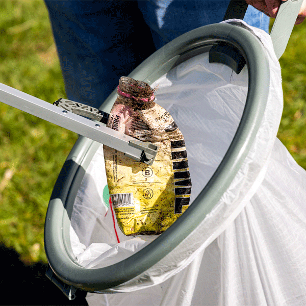 Close-up of a litter picking hoop with rubbish being placed in a plastic bag on a grassy background