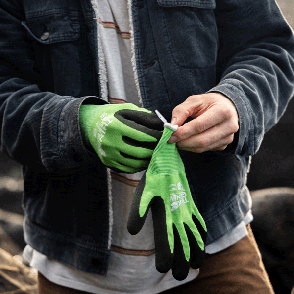 Person wearing green gardening gloves with black gloves underneath, holding a small object.