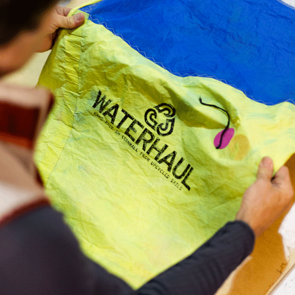 Man holding up a green and blue litter picking bag made from sails with Waterhaul branding