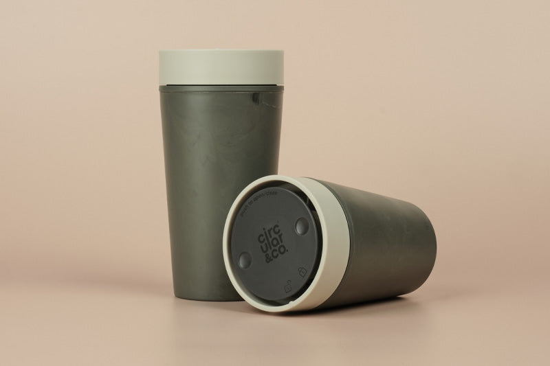 Two green travel mugs with beige lids on a beige background