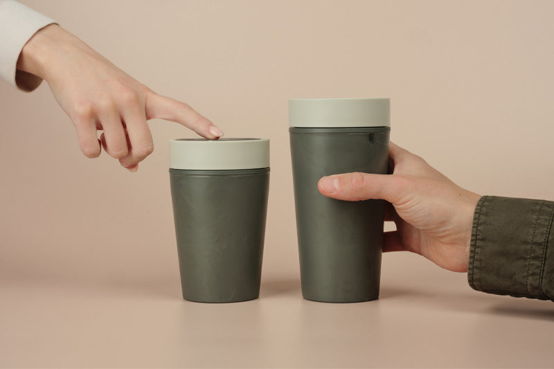 Two green coffee cups with matching lids on a beige background