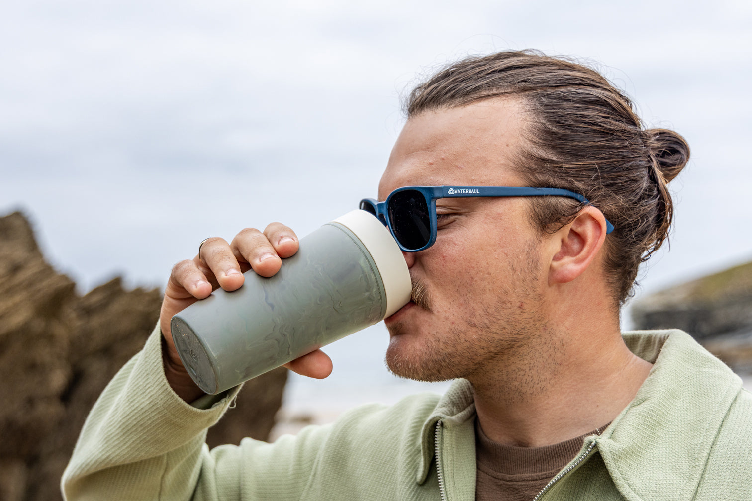 Man drinking from a insulated mug outdoors with sunglasses on