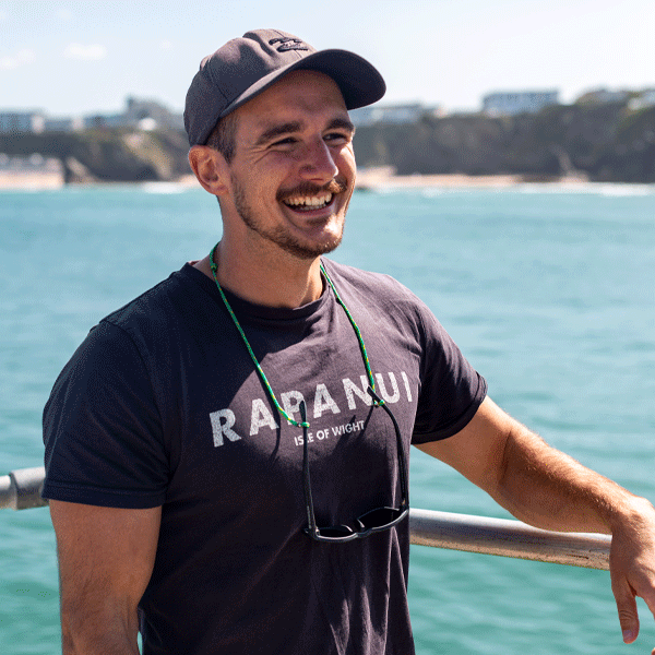 Man wearing a black t-shirt with sunglasses hanging from a glasses chain by the water