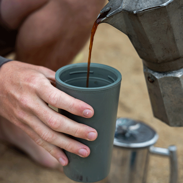 Person pouring coffee from a portable coffee maker into a green cup.