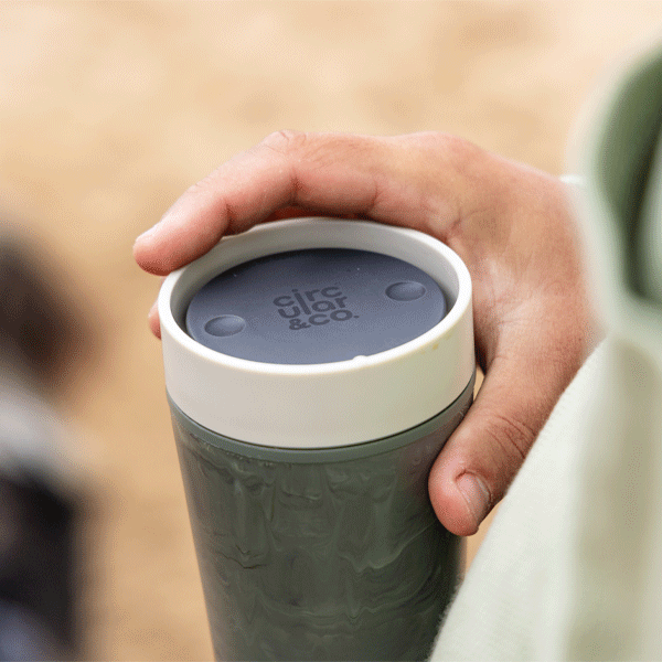 Hand holding a travel mug with 'Circular&Co.' branding on a blurred background