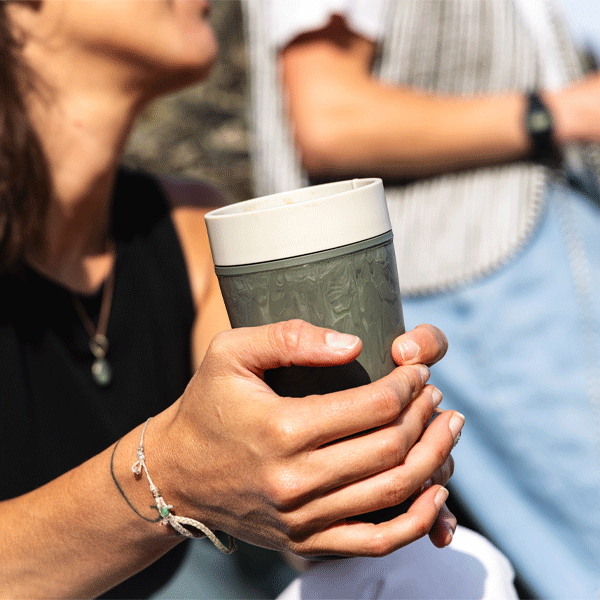 Person holding a green reusable cup outdoors with another person in the background
