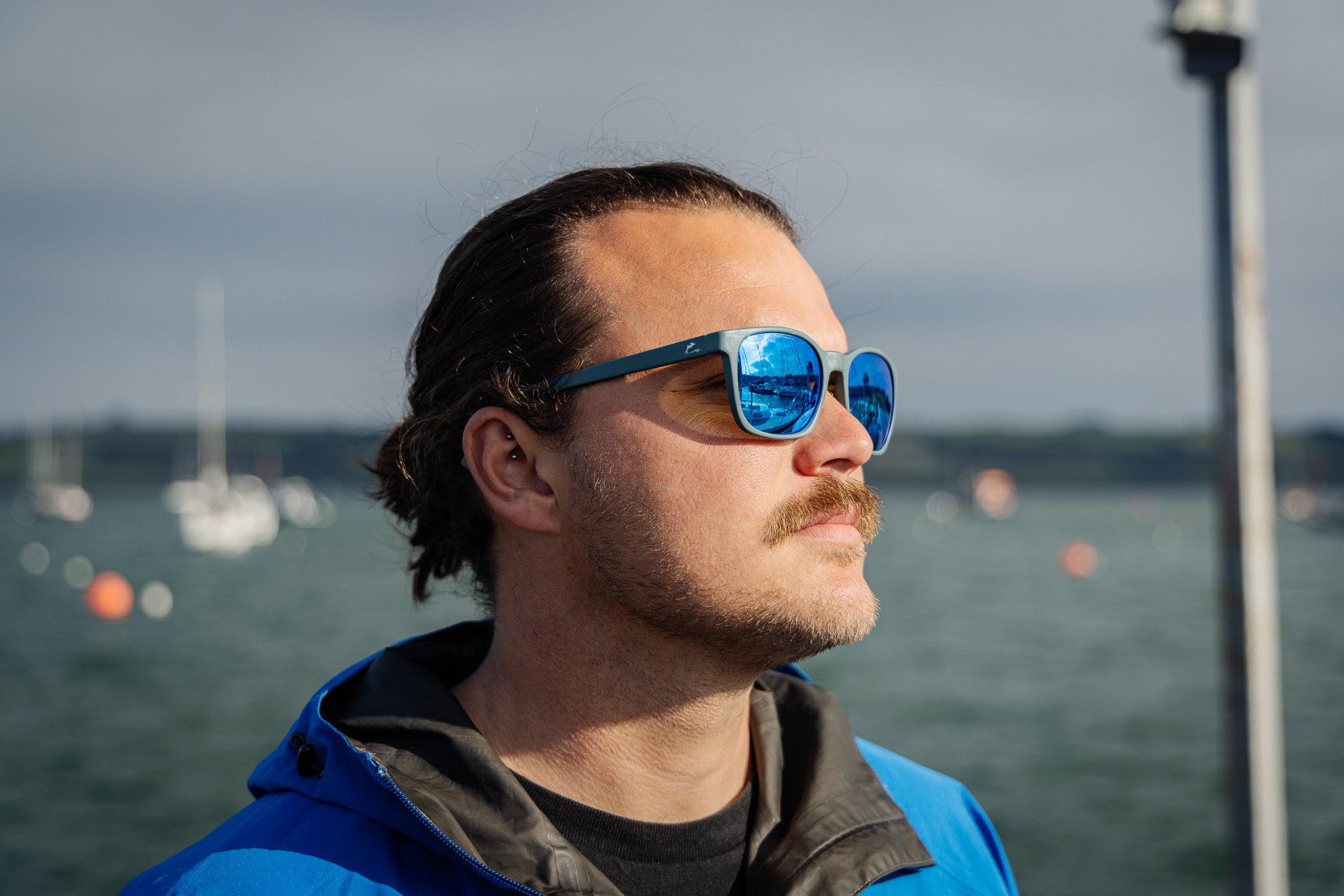 Man wearing sunglasses with blue lenses with a waterfront background.