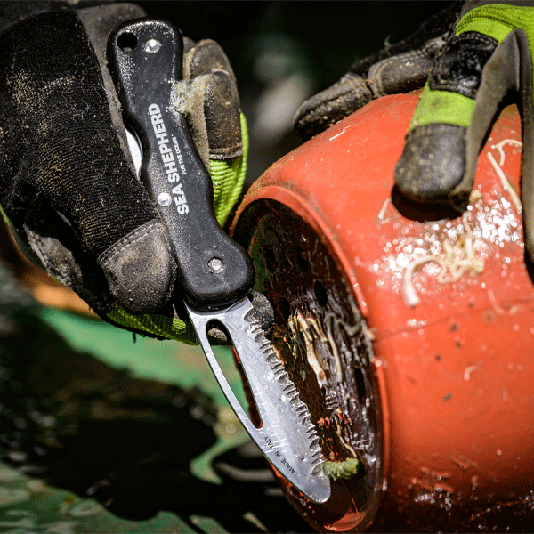 Person using a Sea Shepherd knife on a red object with gloves on