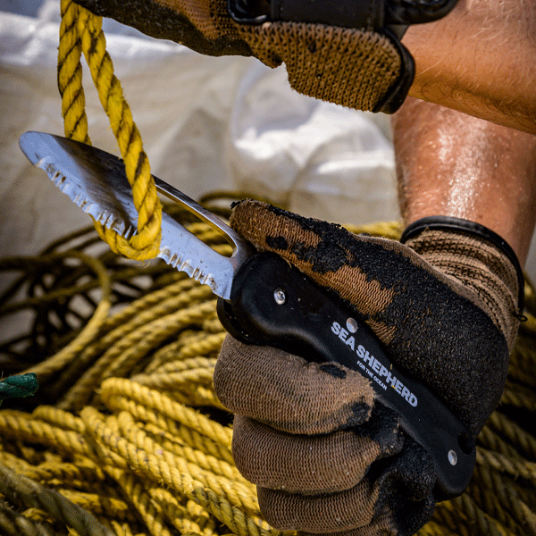 Hand holding a knife with a Sea Shepherd logo amidst fishing nets