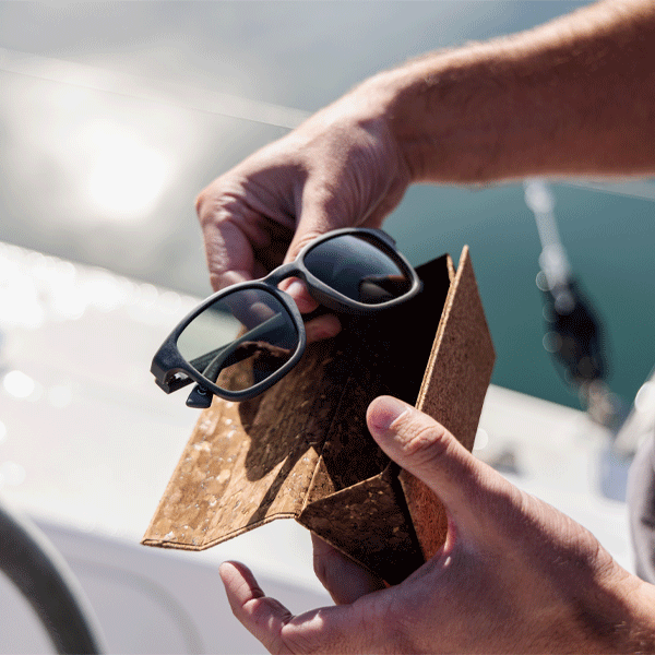 Person holding sunglasses in a cork case with a blurred outdoor background