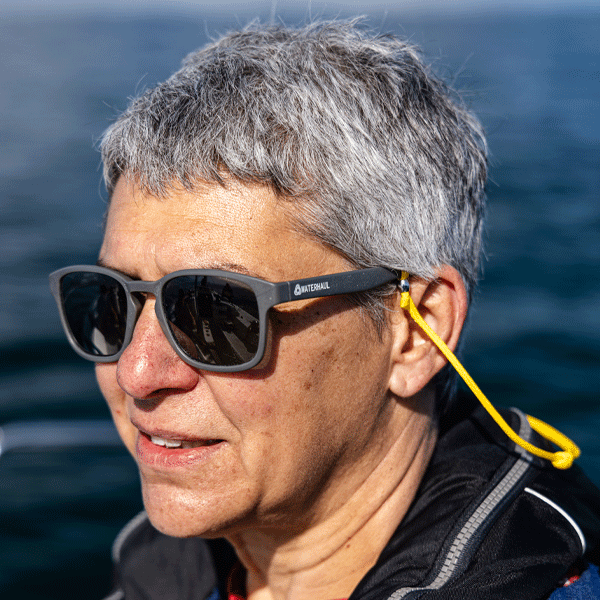 Person wearing sunglasses with a yellow cord, standing against a blue water background